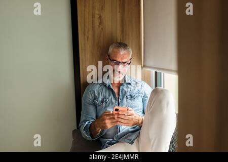 Lächelnder reifer Mann mit Handy im Wohnzimmer an Zu Hause Stockfoto