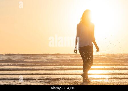 In Silhouette einer Frau, die am Strand Wasser spritzt Bei Sonnenuntergang Stockfoto