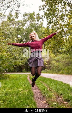 Junge Frau mit ausgestreckten Armen fröhlich springen im Park Stockfoto