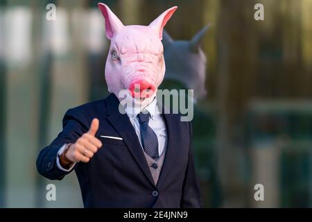Junger Geschäftsmann trägt Schweinemaske und tut Daumen nach oben gegen Büro Gebäude Stockfoto