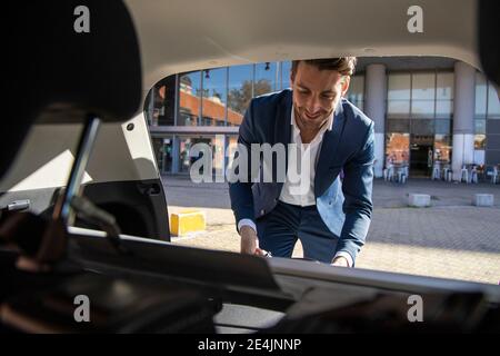 Geschäftsmann mit Gesichtsmaske, der das Gepäck vom Kofferraum des Taxis nimmt Stockfoto