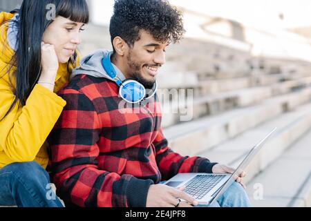 Junges Paar lächelt, während mit Laptop sitzen im Freien Stockfoto