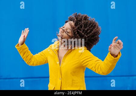 Lächelnde Frau, die Haare wirft, während sie gegen die blaue Wand tanzt Stockfoto