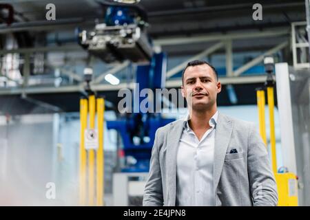 Lächelnder reifer Geschäftsmann im Anzug, der in der Fabrik steht Stockfoto