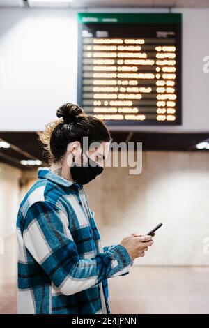 Mann trägt Schutzmaske mit Handy im Stehen An der U-Bahn-Station Stockfoto