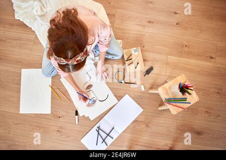 Künstlerin zeichnet, während sie auf dem Boden im Wohnzimmer sitzt Stockfoto