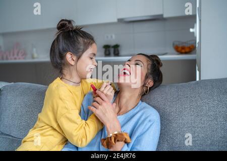 Lächelnde Tochter Anwendung Lippenstift auf Mutter im Wohnzimmer an Zu Hause Stockfoto