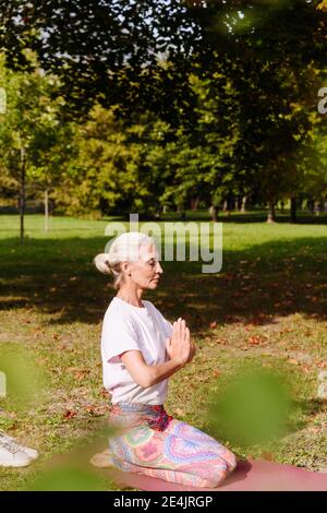 Reife Frau tut Yoga-Übung auf Gras im öffentlichen Park Stockfoto