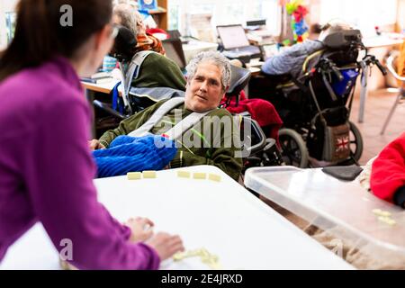 Behinderter Mann, der die Krankenschwester beim Spielen von Domino in der Krankenpflege ansieht Zu Hause Stockfoto
