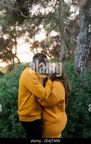 Mann trägt Gesichtsmaske küssen Frau, während im Wald stehen Stockfoto