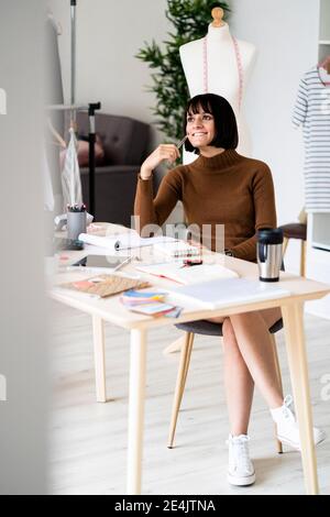 Lächelnde Stylistin, die neue Designs in ihrem Atelier in Betracht zieht Stockfoto