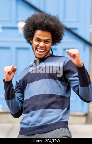 Aufgeregt junger Mann mit lockigen Haaren gestikulierenden beim Stehen gegen Wand Stockfoto