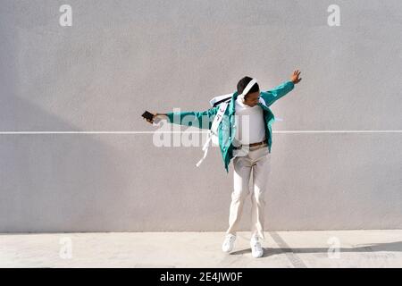 Sorgloser Mann mit Kopfhörern und Handy, der mit Armen tanzt Ausgestreckt gegen graue Wand Stockfoto