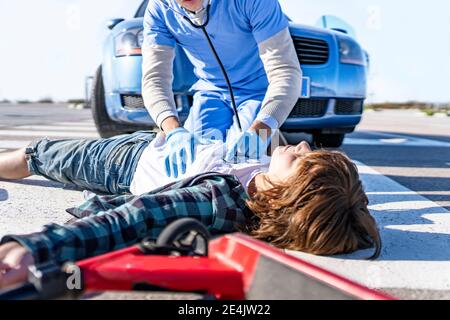 Männlicher Rettungsarbeiter mit Stethoskop, der Jungen auf der Straße untersucht Nach einem Autounfall Stockfoto