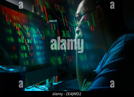 Nahaufnahme asiatischer Mann mittleren Alters, der das Candlestick-Graph-Diagramm der Aktienmarktanlagen analysiert, die ernsthaft in einem Raum mit wenig Licht gehandelt werden, Effektdesign für Stockfoto