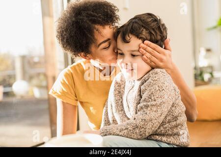 Mutter küsst Sohn, während sie zu Hause sitzt Stockfoto