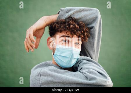 Mann mit erhobener Hand trägt OP-Maske vor grünem Hintergrund Im Studio Stockfoto