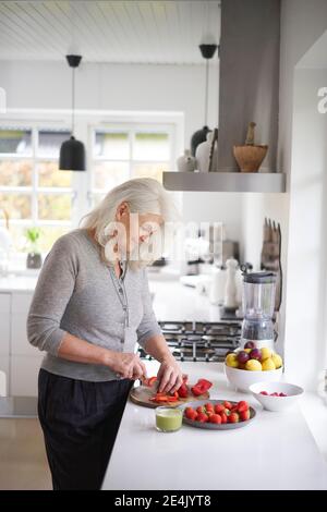 Rentner ältere Frau schneiden Erdbeeren in der Küche zu Hause Stockfoto