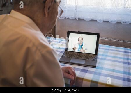 Älterer Mann, der auf Video Ratschläge von einem männlichen Hausarzt einnahm Durch Laptop im Wohnzimmer Stockfoto