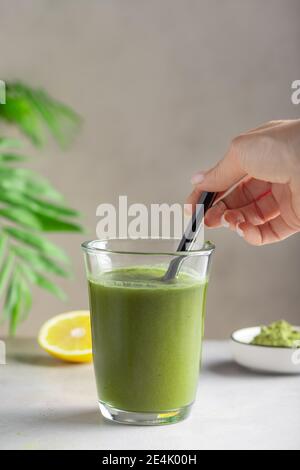 Weibliche Hand, die Wasser mit grünem Superfood Pulver mischt Stockfoto