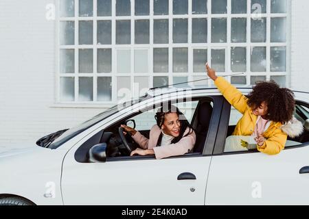 Lächelnde Mutter, die Tochter anschaut, die im Auto durch das Fenster guckt Stockfoto