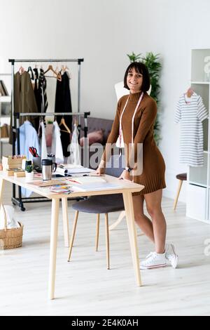 Lächelnde junge Modedesignerin mit Maßband um den Hals Im Atelier Stockfoto