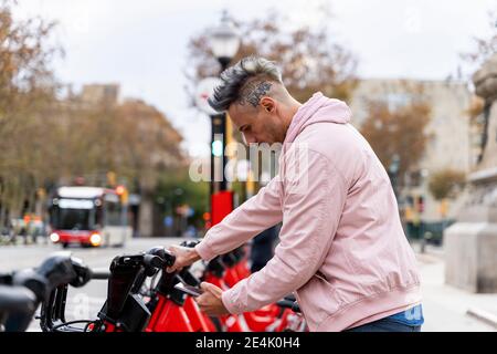 Stilvoller Mann, der am Parkplatz ein Fahrrad über ein Smartphone ausleihen konnte Stockfoto