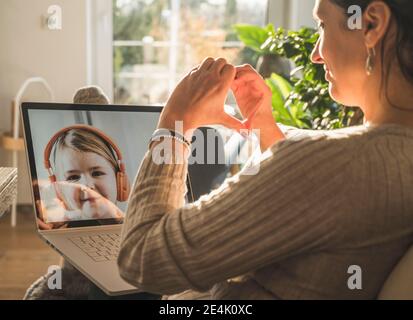 Frau macht Herzform mit Händen während Videoanruf mit Kleines Mädchen Stockfoto