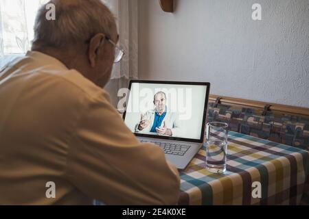 Älterer Mann, der vom männlichen Hausarzt über einen Laptop Rat einnahm Videoanruf zu Hause Stockfoto