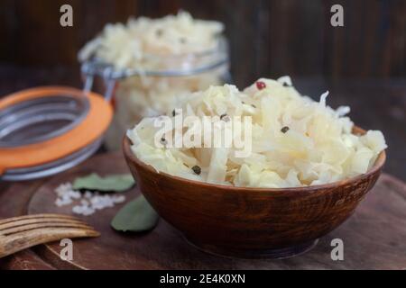 Hausgemachtes Sauerkraut mit schwarzem und rotem Pfeffer in Holzschüssel auf rustikalem Hintergrund. Gesunde probiotische Nahrung im Winter. Stockfoto