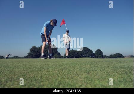 Freunde spielen Golf gegen klaren blauen Himmel auf Platz Stockfoto
