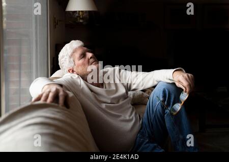 Älterer Mann mit geschlossenen Augen, der sich entspannt, während er auf dem Sofa sitzt Zu Hause Stockfoto