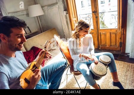 Glückliches junges Paar spielt Duett mit Schlagzeug und Gitarre in Wohnzimmer zu Hause Stockfoto