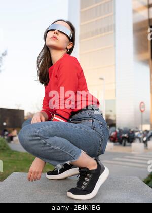 Junge Frau mit Sonnenbrille hocken auf dem Fußweg in der Stadt Stockfoto