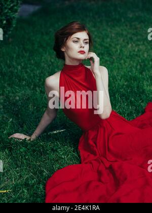 Frau in roten Kleid sitzt auf dem Gras Charme und Luxuriöser Park im exotischen Stil Stockfoto