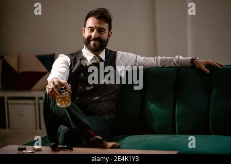 Porträt von bärtigen Mann sitzt auf dem Sofa mit Glas Whiskey in der Hand Stockfoto