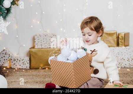 Baby-Mädchen hält Weihnachtslichter in Geschenkbox während des Sitzens Zu Hause Stockfoto