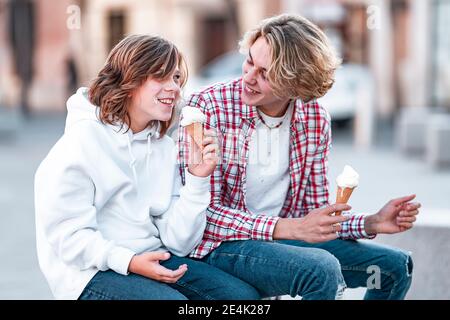 Lächelnder Junge, der Eis isst, während er im Freien bei einem Mann sitzt Stockfoto