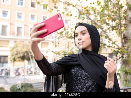 Portrait der jungen schönen Frau trägt schwarzen Hijab unter Smartphone Selfie Stockfoto