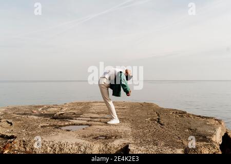 Junger Mann, der sich zurückbeugt, während er auf dem Pier am Meer steht Stockfoto