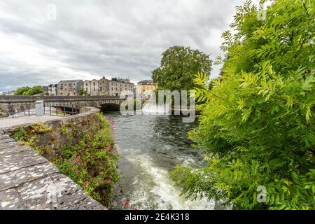 Galway, Connacht Provinz, Irland. Juni 11, 2019. Blick auf den Fluss Corrib und die William O'Brien Brücke, das Wasser fließt ruhig, eine kleine Staumauer Form Stockfoto