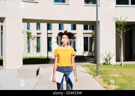 Universitätsstudentin hält Bücher, während sie mit geschlossenen Augen steht universität Stockfoto