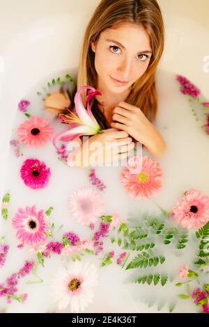 Lächelnde Frau, die in der Badewanne lag, während sie im Spa ein Milchbad nahm Stockfoto