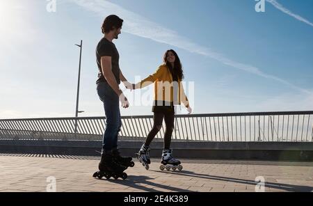 Glückliches junges Paar, das sich beim Skaten auf dem Pier die Hände hält