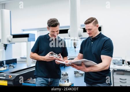 Männliche Techniker mit Maschinenteil lesen Bedienungsanleitung in der Industrie Stockfoto