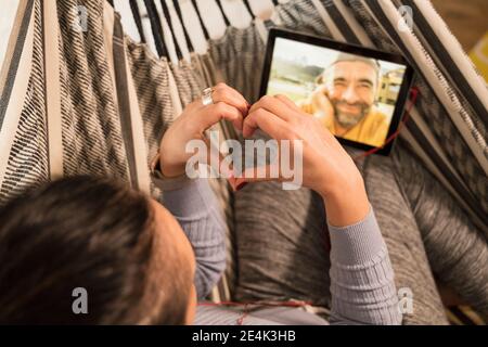 Reife Frau zeigt Herzform Zeichen auf Videoanruf zu Mensch durch digitales Tablet Stockfoto