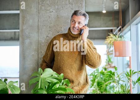 Mann, der auf dem Handy spricht, während er sich auf die Säule stützt Büro Stockfoto