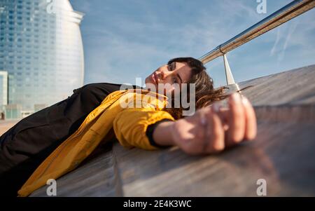 Sorglose Frau, die bei Sonnenschein auf der Stützmauer am Pier liegt Tag Stockfoto