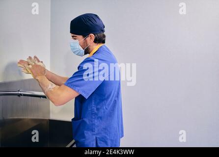 Männliche Arzt trägt Gesichtsmaske waschen Hände während des Stehens an Krankenhaus Stockfoto