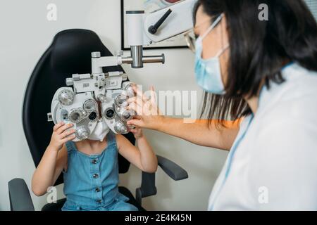 Weibliche Optometristin untersucht Mädchen Augen durch Propther in der Klinik während COVID-19 Stockfoto